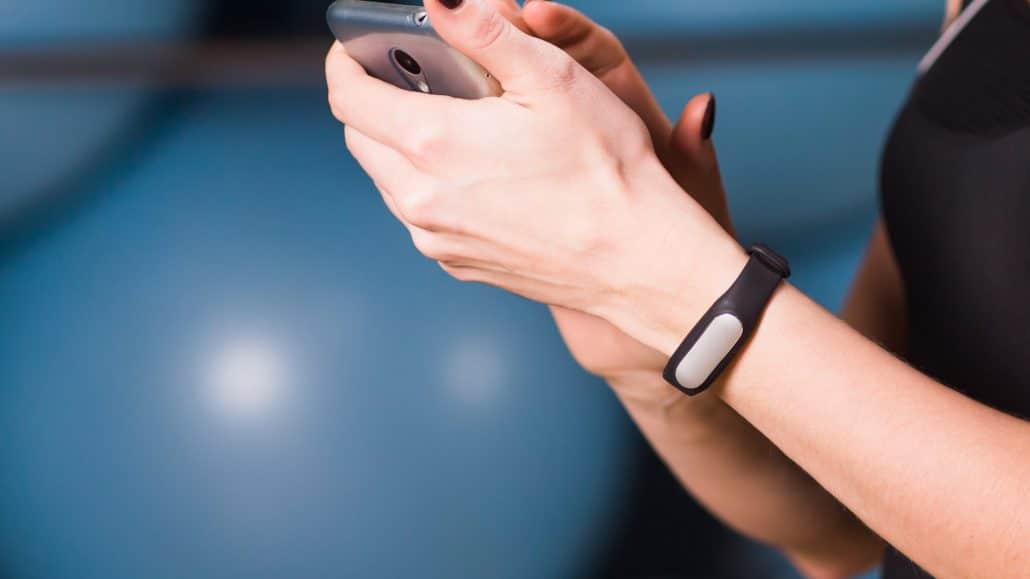 Hände nutzen ein Smartphone mit Fitnessarmband