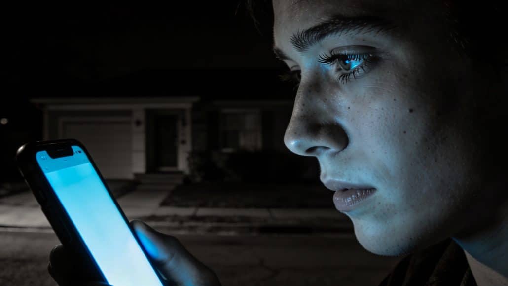 Junge betrachtet sein Handy in der Dunkelheit.